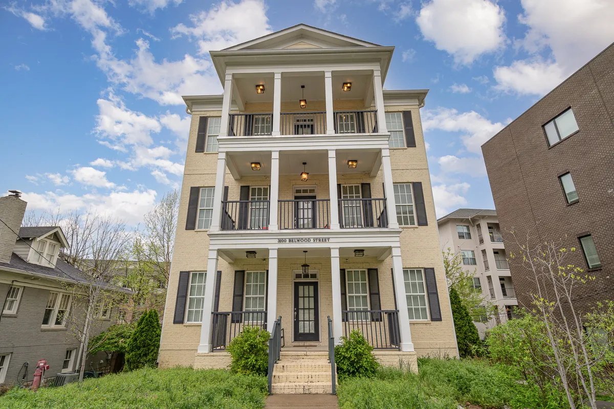 This image displays the front facade of the Belwood Bloom building with its welcoming porch and symmetrical windows, set in a peaceful exterior environment. The porch is inviting, suggesting a perfect spot to relax outdoors, possibly with a pet by your side.