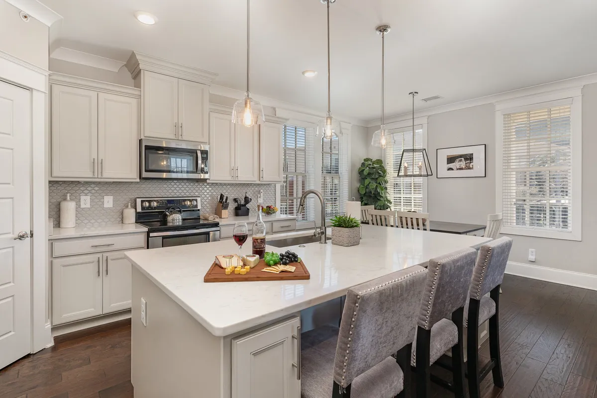 A stylish, contemporary kitchen island adorned with a display of cheese and wine, flanked by modern appliances and pendant lights. Large windows flood the kitchen with daylight, making it ideal for entertaining or casual family gatherings.