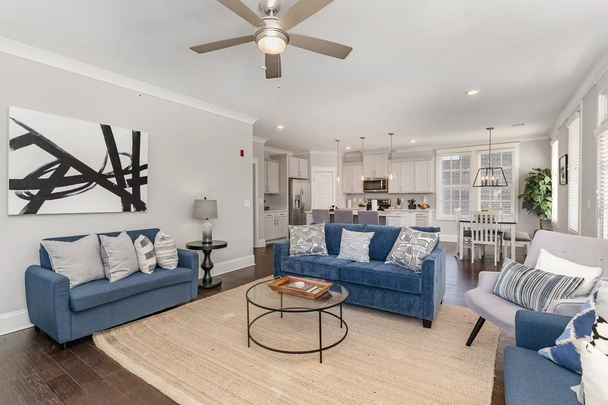 The image showcases a spacious, stylish living area with a comfortable sofa, chic coffee table, eye-catching artwork, and an open kitchen in the background. The space feels inviting and perfect for group gatherings, whether you’re sharing a meal, relaxing with friends, or curling up with a good book.