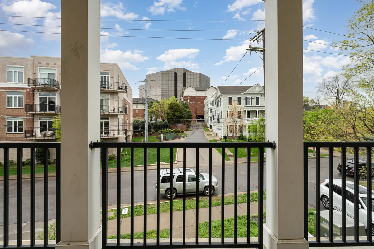 A peaceful view from a balcony, overlooking the street and nearby buildings, suggesting moments of relaxation and connection to the surrounding neighborhood. The image embodies the idea of enjoying coffee or group conversations while watching the activity beyond the property.