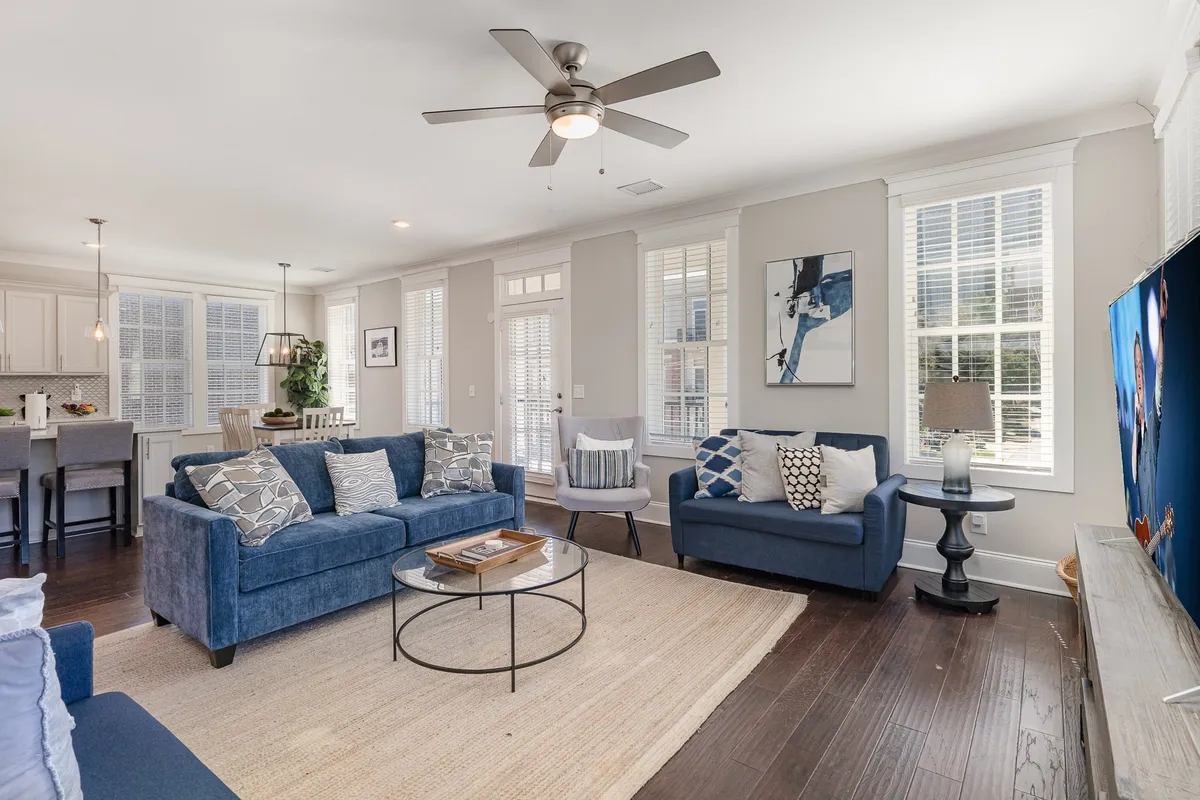 A spacious living room set up for both relaxation and entertaining, featuring a coordinated sofa set, a large coffee table, a television, and artwork on the wall. The open arrangement allows for easy movement and group interaction.