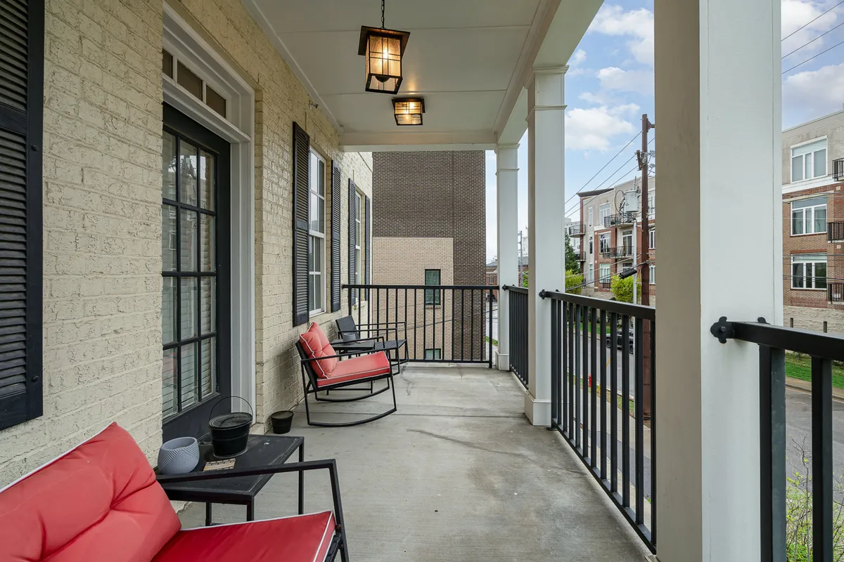 This photo features a similar balcony scene to the previous image, with red chairs, black railing, and hanging lanterns. The perspective is slightly different, emphasizing the cozy seating arrangement and the inviting ambiance for socializing or enjoying peaceful moments outdoors.