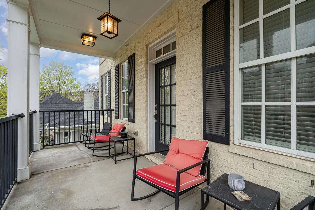 This image shows an exterior balcony setting featuring red chairs, black railing, hanging lanterns, and large windows. The mood is relaxed, suggesting a perfect spot for morning coffee, evening relaxation, or reading a book outdoors. The space is inviting, stylish, and clearly designed for comfort and social connection.