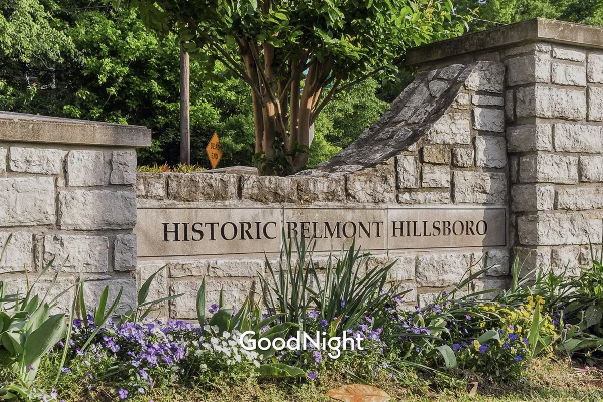 A historic stone sign surrounded by colorful flowers and lush greenery, evoking the feeling of community parks and outdoor gathering spots. The setting is perfect for daily dog walks and enjoying nature close to home.