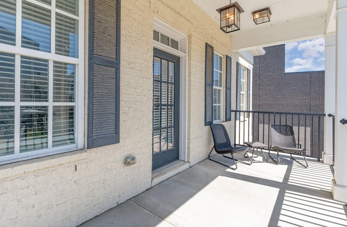 An inviting exterior porch with chairs, shutters, and warm lighting fixtures, set against the home's front door. The mood is relaxed and homey, ideal for enjoying morning coffee, reading, or watching the sunset. The setup caters to both solo relaxation and social moments.